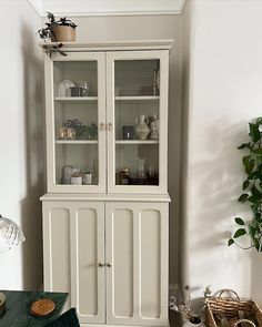 a white china cabinet with glass doors in a living room next to a potted plant