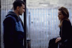 a man and woman standing next to each other in front of a fenced area