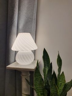 a white lamp sitting on top of a table next to a green potted plant