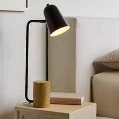 a black lamp sitting on top of a wooden block next to a white bed with pillows