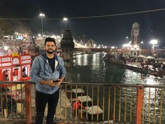 a man standing next to a river at night with lots of lights on the water