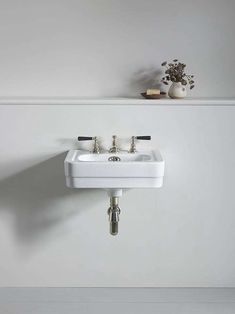 a white sink sitting on top of a wall next to a vase filled with flowers