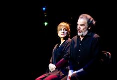 a man and woman sitting next to each other on a chair in front of a black background