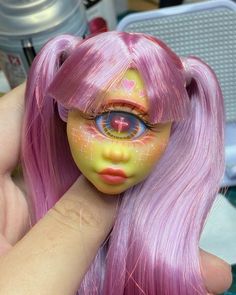 a close up of a person holding a doll with long pink hair and big eyes