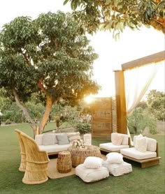 an outdoor seating area with wicker furniture and pillows on the grass in front of a tree