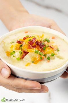 a person holding a bowl of soup with bacon and green onions in it, ready to eat