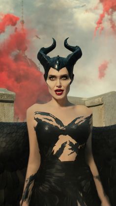 a woman dressed as maleficent stands in front of a red cloud filled sky