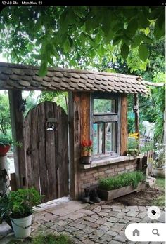 a small wooden shed with a cat sleeping in the window and potted plants outside