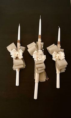 three white candles with bows on them sitting next to each other in front of a black background