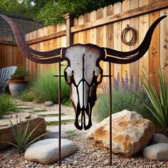 a metal cow skull sitting on top of a rock covered ground next to a wooden fence