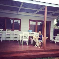 a little boy that is standing on a porch with a dog in front of him