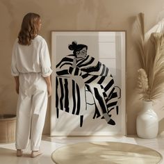 a woman standing in front of a black and white painting next to a potted plant