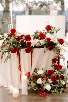 red and white flowers are arranged on the back of a wedding ceremony arch with candles