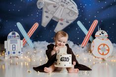 a baby sitting in front of a cake with star wars decorations on the wall behind it