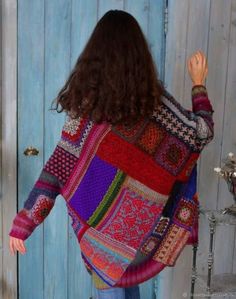 a woman standing in front of a blue door wearing a multicolored cardigan