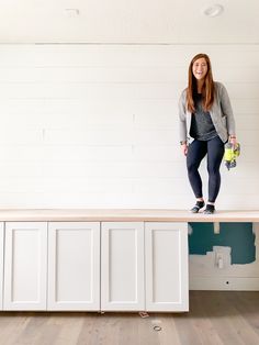 a woman standing on top of a counter in a room with white walls and wood floors