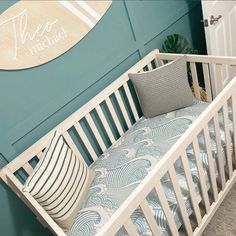 a white crib with a blue and white pillow on it in front of a green wall