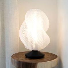 a white lamp sitting on top of a wooden table next to a curtained window