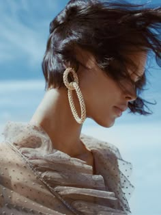 a woman with long hair wearing large gold hoop earrings on her head and looking off into the distance