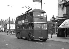 a black and white photo of a double decker bus driving down the street in an old town