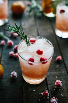 a drink with cranberries and rosemary garnish sits on a wooden table