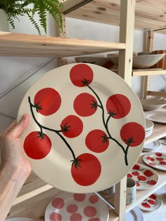 a person holding up a plate with red tomatoes on it in front of shelves full of plates