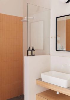 a white sink sitting under a bathroom mirror next to a wooden cabinet and counter top