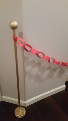 a pole with a pink ribbon on it next to a white wall and wooden floor