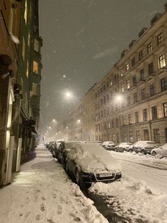 cars parked on the side of a snow covered street in front of tall buildings at night