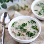 two white bowls filled with soup on top of a table next to a spoon and napkin