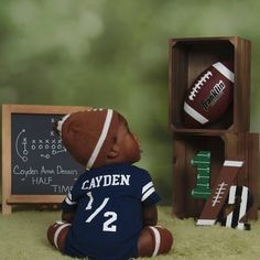 a baby doll sitting in front of a wooden box with footballs and chalkboard