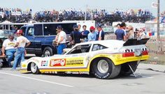 a drag car is parked on the side of the road in front of a crowd