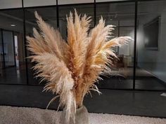 a vase filled with lots of dry grass in front of a glass wall and door