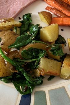 a white plate topped with potatoes and spinach next to carrots on top of a table