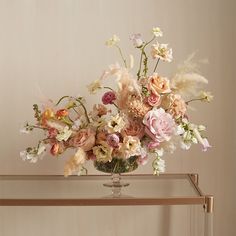 a vase filled with lots of flowers sitting on top of a glass table next to a wall