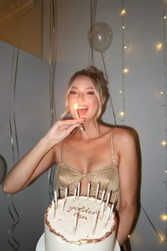 a woman holding a lit candle up to her mouth while standing in front of a cake