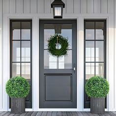 two potted plants sitting on the front steps of a house, with a wreath hanging over the door