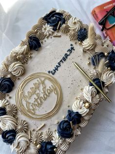 a birthday cake decorated with blue flowers and gold trimmings on top of a table