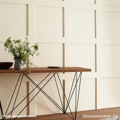 a wooden table topped with a vase filled with white flowers next to a wall mounted panel