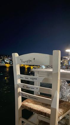 a white wooden chair sitting on top of a pier next to the ocean at night