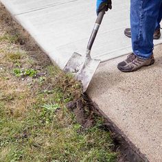 a person with a shovel digging in the ground next to a sidewalk that has grass growing on it