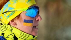 a woman with her face painted in the colors of the ukraine flag and wearing skis