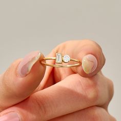 a woman's hand holding a gold ring with two stones on it and a diamond in the middle