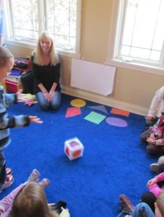 a group of children sitting on the floor in front of a woman playing with blocks