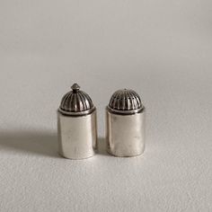 two silver salt and pepper shakers on a white surface