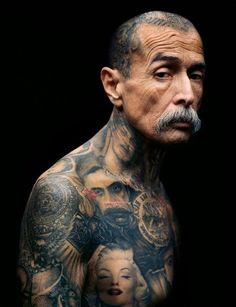 an older man with tattoos on his chest and shoulder is looking at the camera while he stands in front of a black background