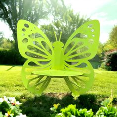 a green butterfly sculpture sitting on top of a lush green park bench surrounded by flowers