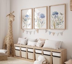 a white room with three pictures on the wall and a stuffed giraffe in the corner