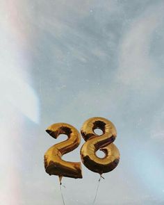 two gold balloons shaped like the number twenty eight are floating in the air against a cloudy blue sky