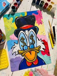 a painting of a ducky with dollar signs on it's face, surrounded by paintbrushes and other art supplies